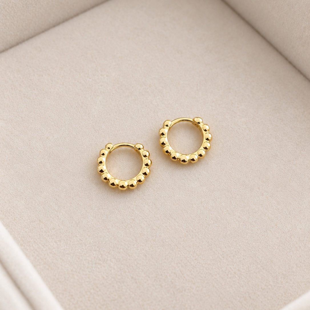 Pair of petite gold coloured 925 silver beaded hoops on cream velvet