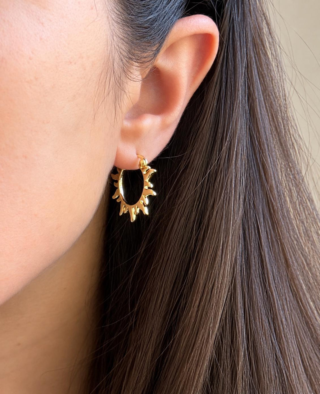 Gold sun-shaped statement hoop earring worn on ear