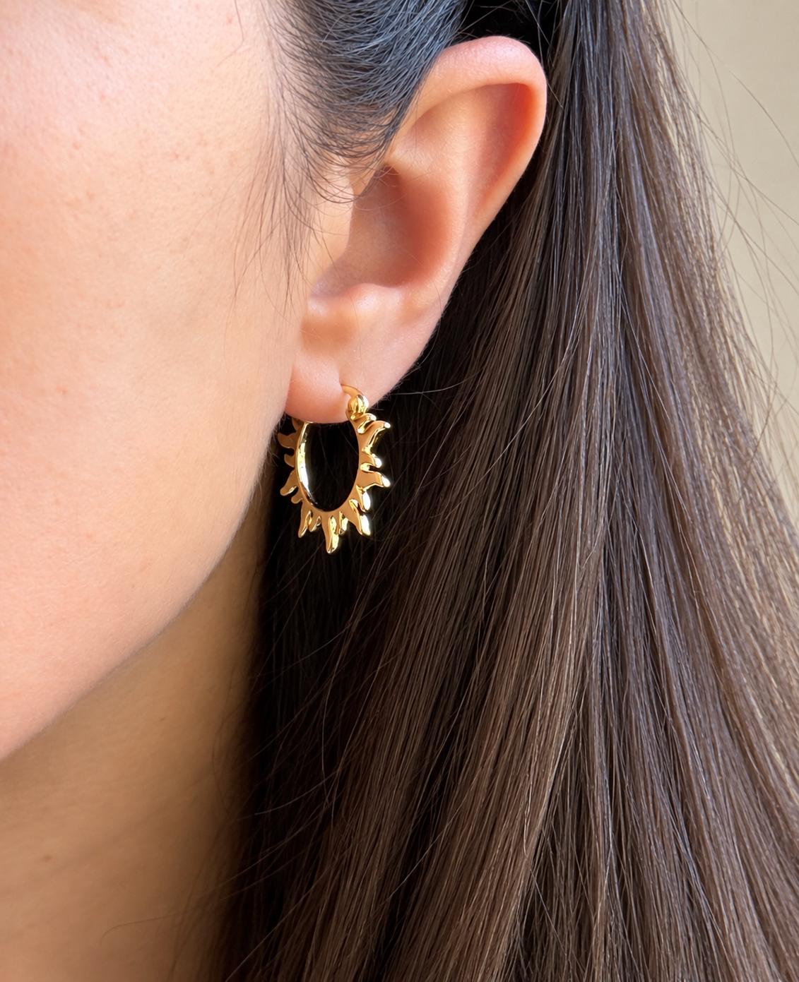 Gold sun-shaped statement hoop earring worn on ear