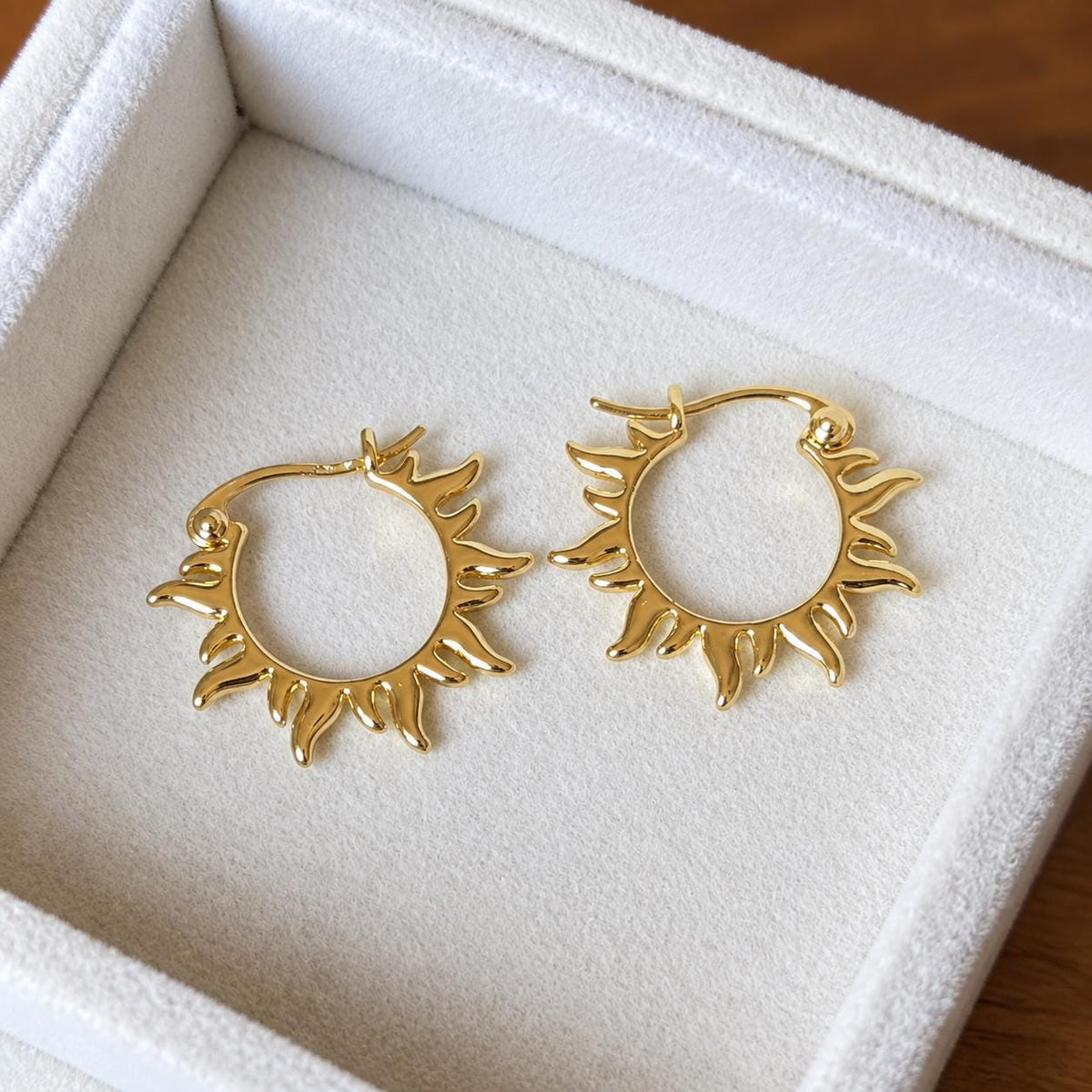 Pair of gold plated sunray hoop earrings on ivory velvet