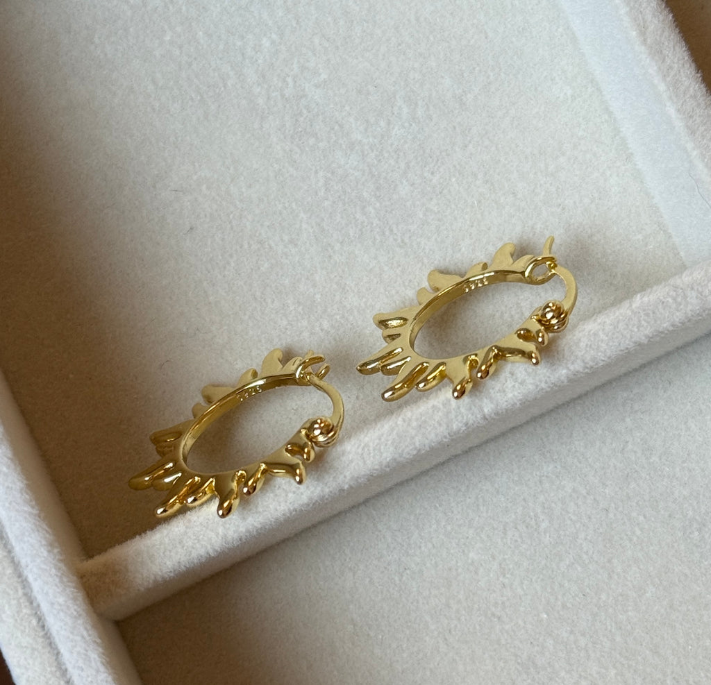 Side view of gold plated sunburst hoop earrings on velvet