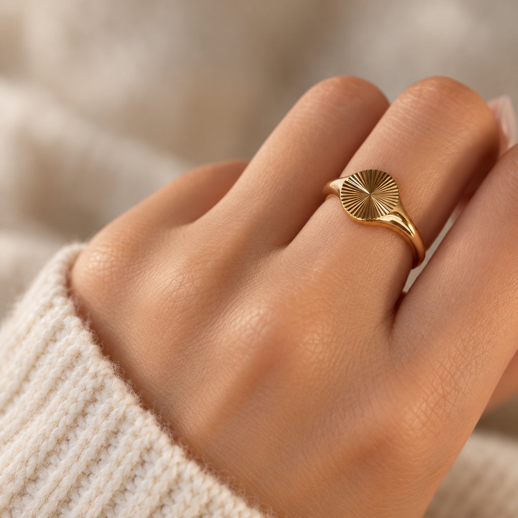 Polished gold sunburst signet ring worn on finger in soft lighting
