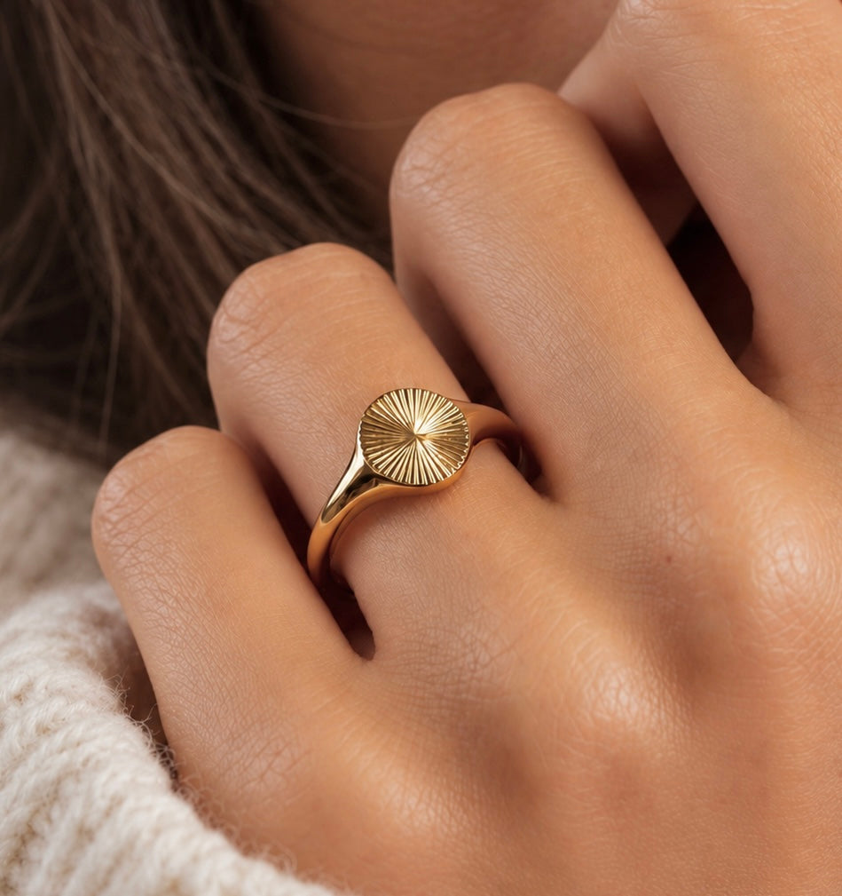 Gold sunburst signet ring with engraved radial sunburst detail worn on hand