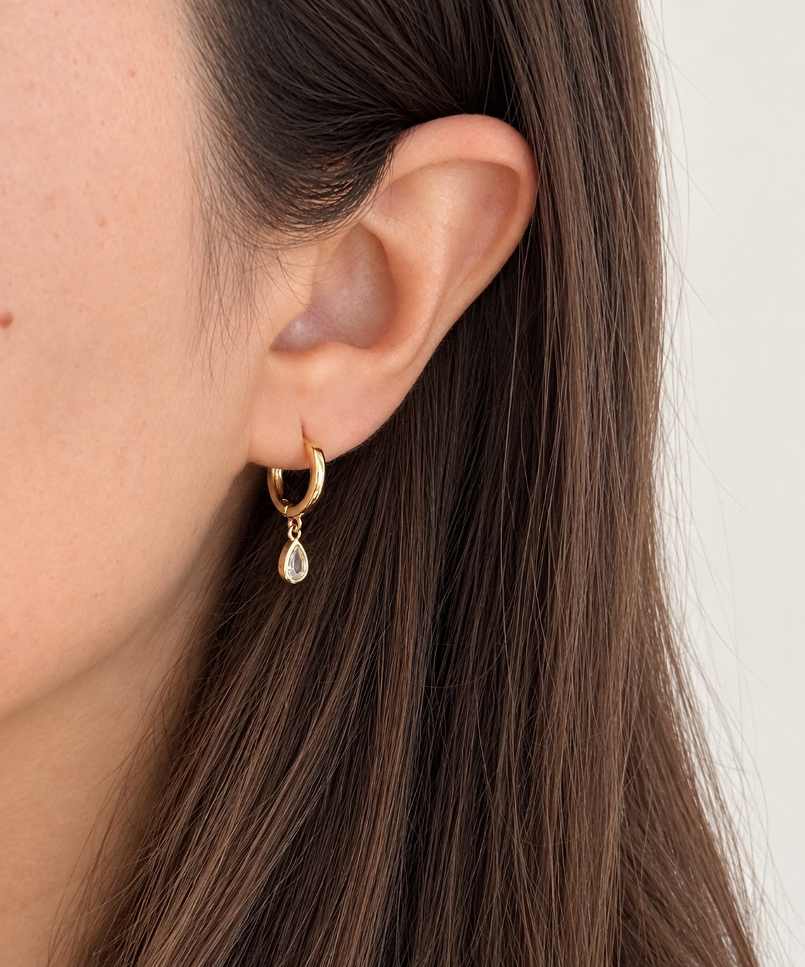 Gold teardrop CZ huggie earring worn on the ear