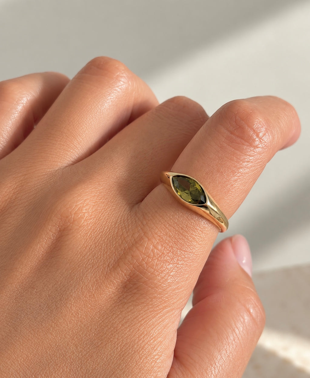 Gold-plated marquise ring with olive green stone worn on finger