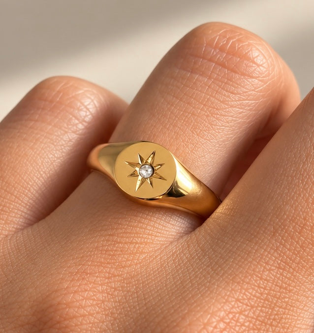 Close-up view of gold signet ring featuring engraved starburst and clear centre stone