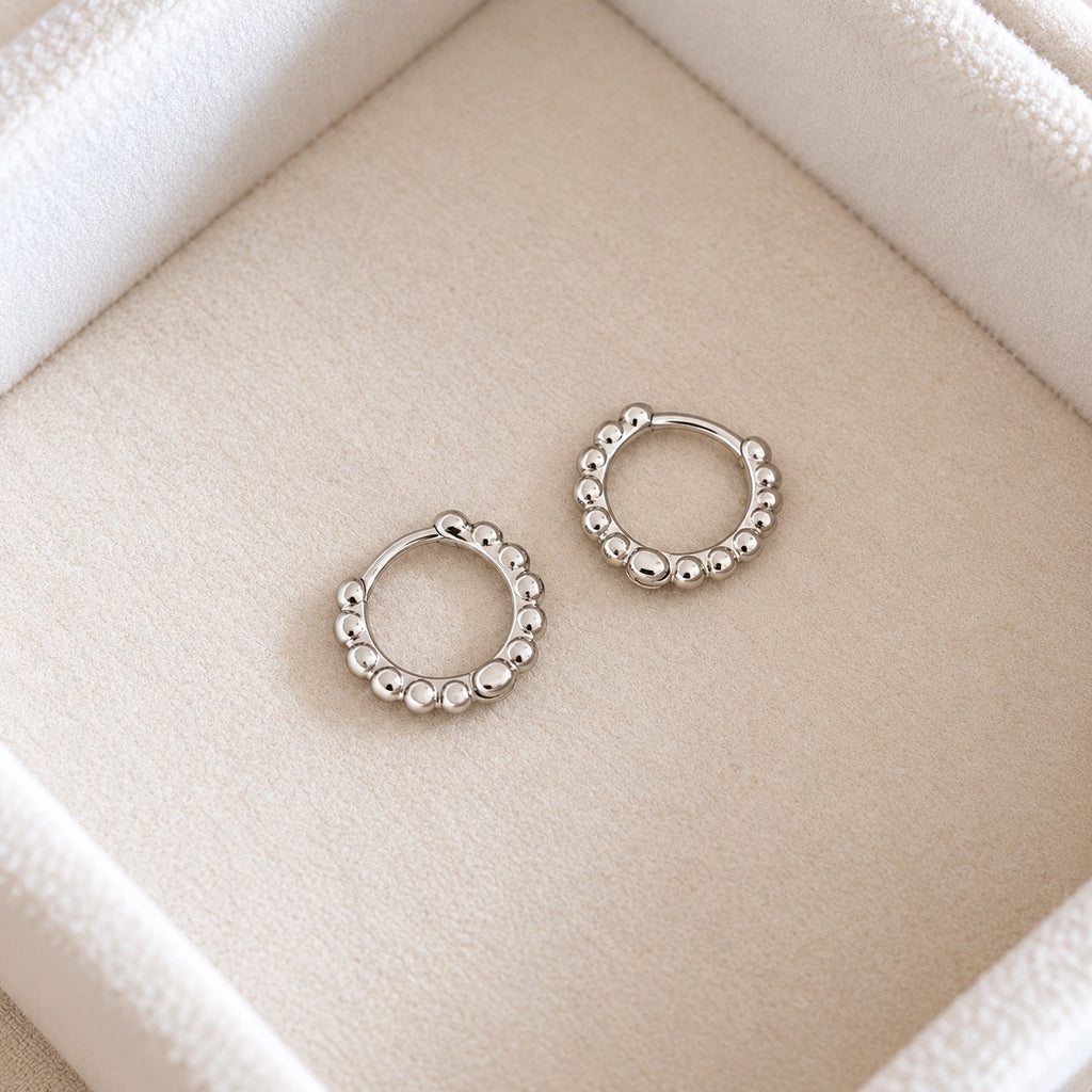 Angled view of silver beaded huggie earrings