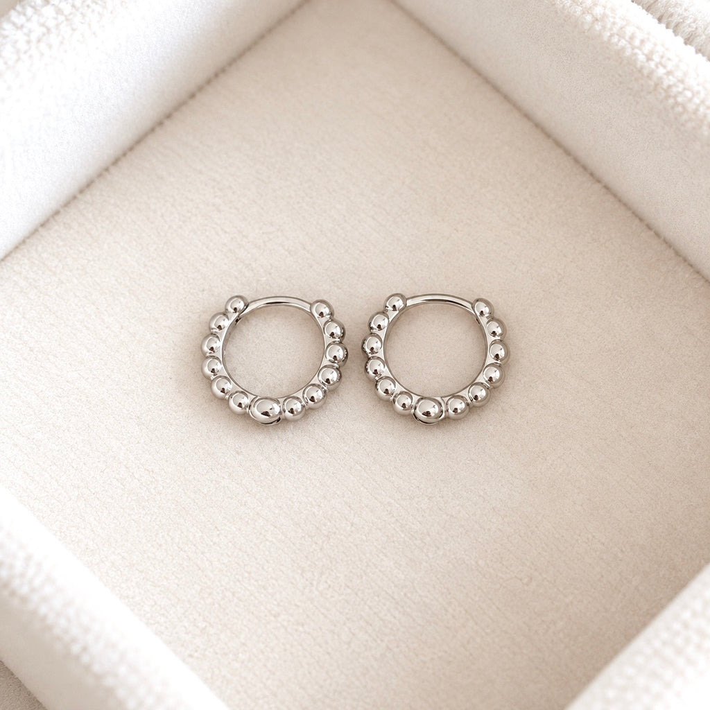 Pair of petite sterling silver beaded huggie hoop earrings on cream velvet