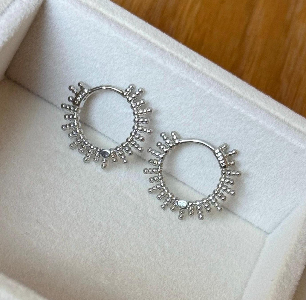 Detailed close-up of silver beaded sunburst hoop earrings in a jewellery box