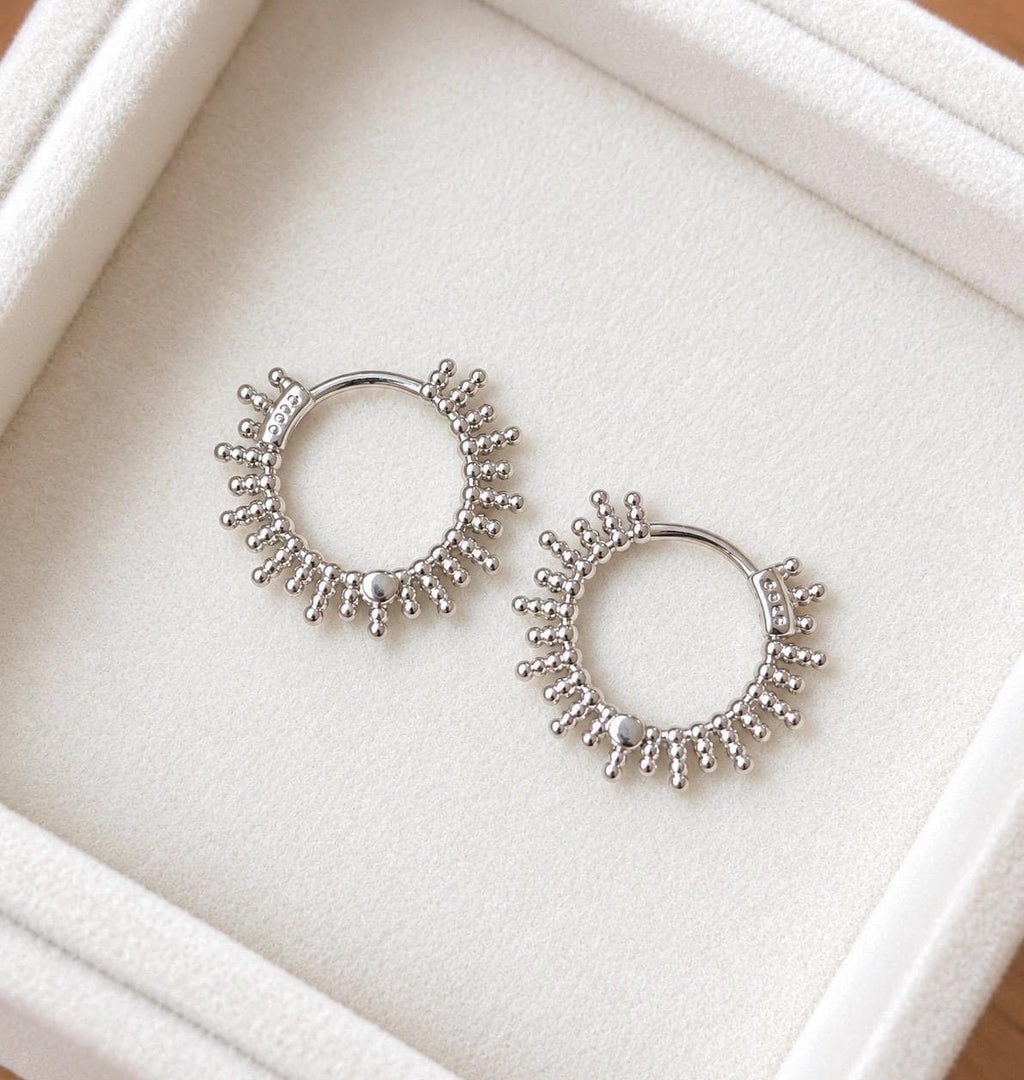 Pair of 925 sterling silver beaded sunburst hoop earrings on an ivory jewellery tray