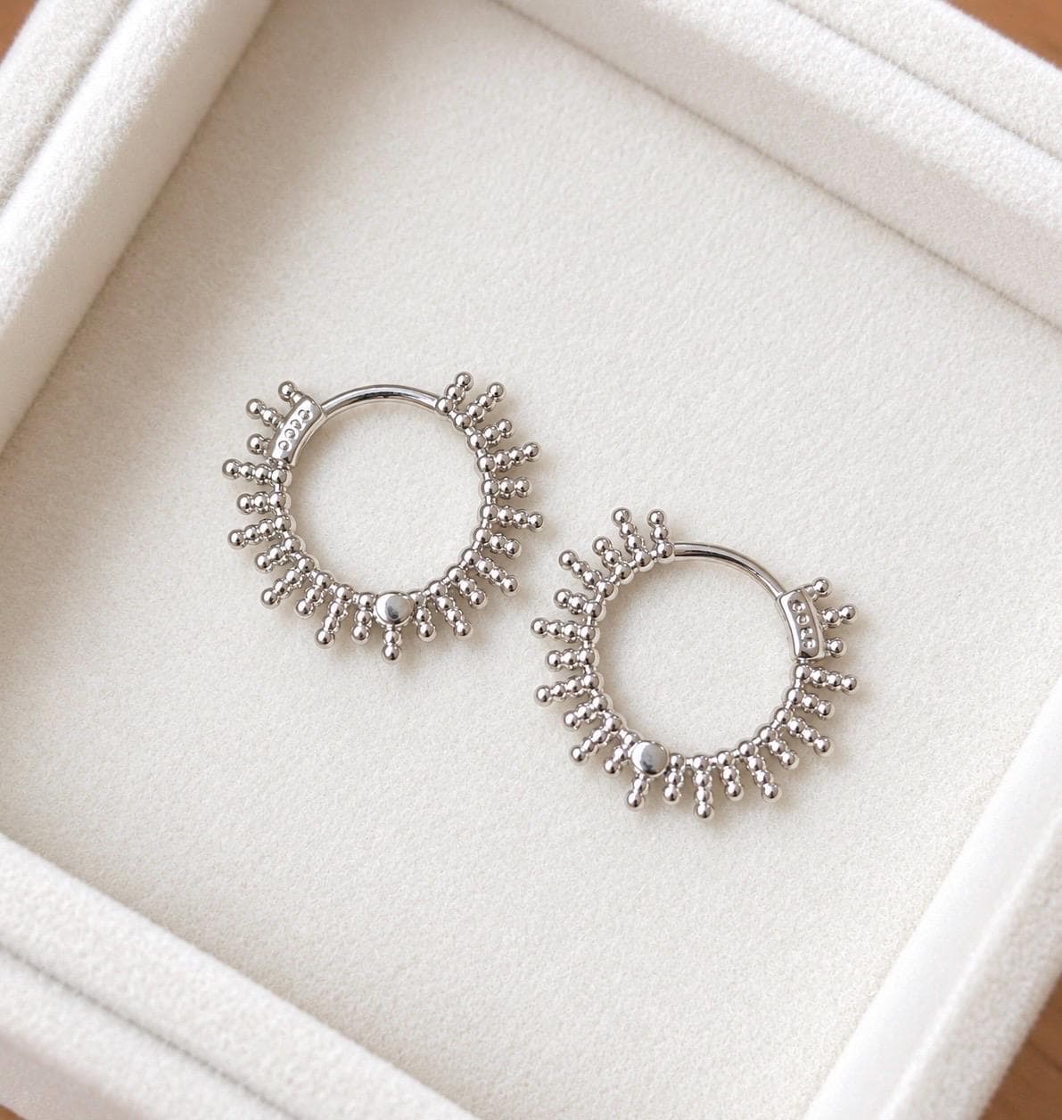 Pair of 925 sterling silver beaded sunburst hoop earrings on an ivory jewellery tray