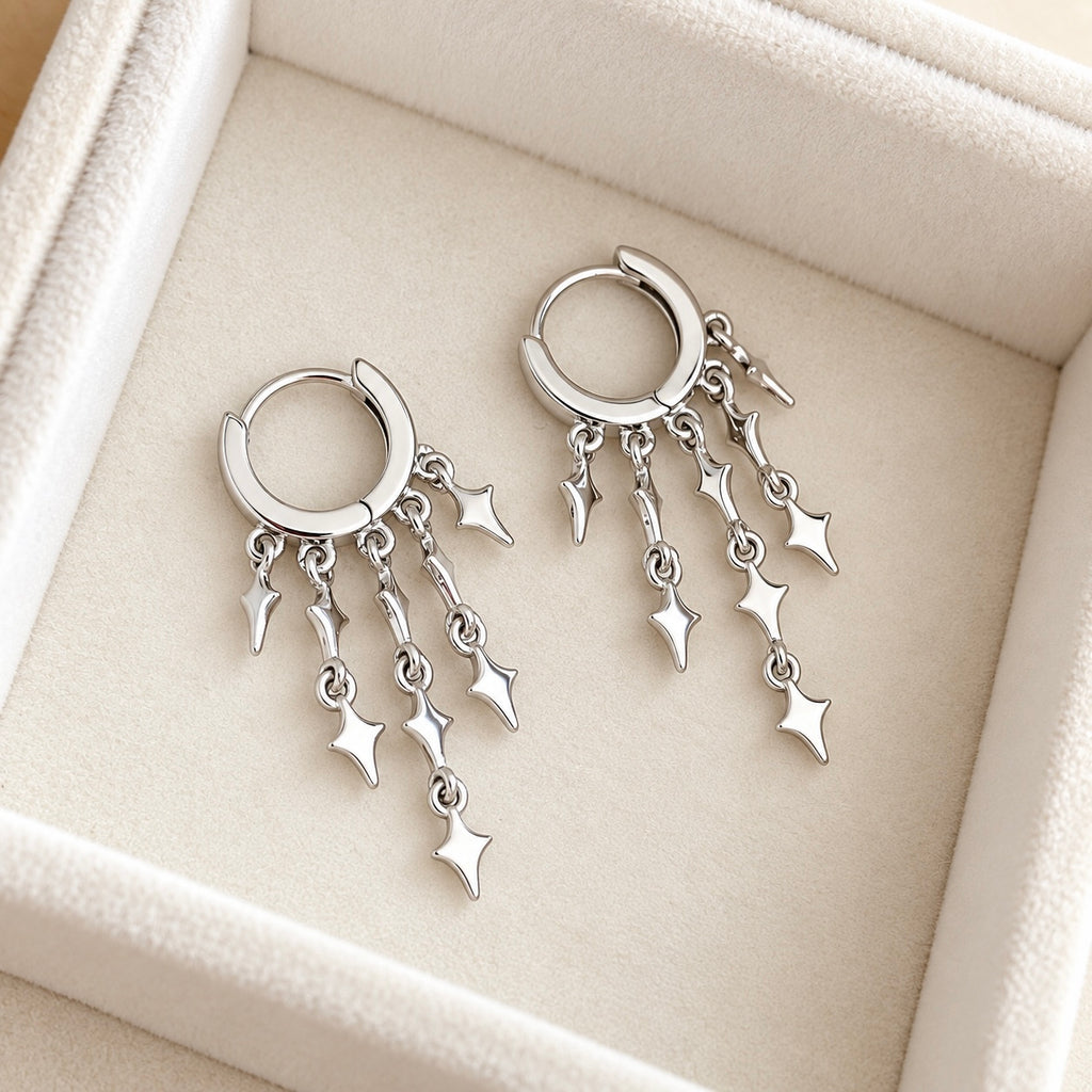 Pair of cascading silver star charm hoop earrings presented on ivory velvet