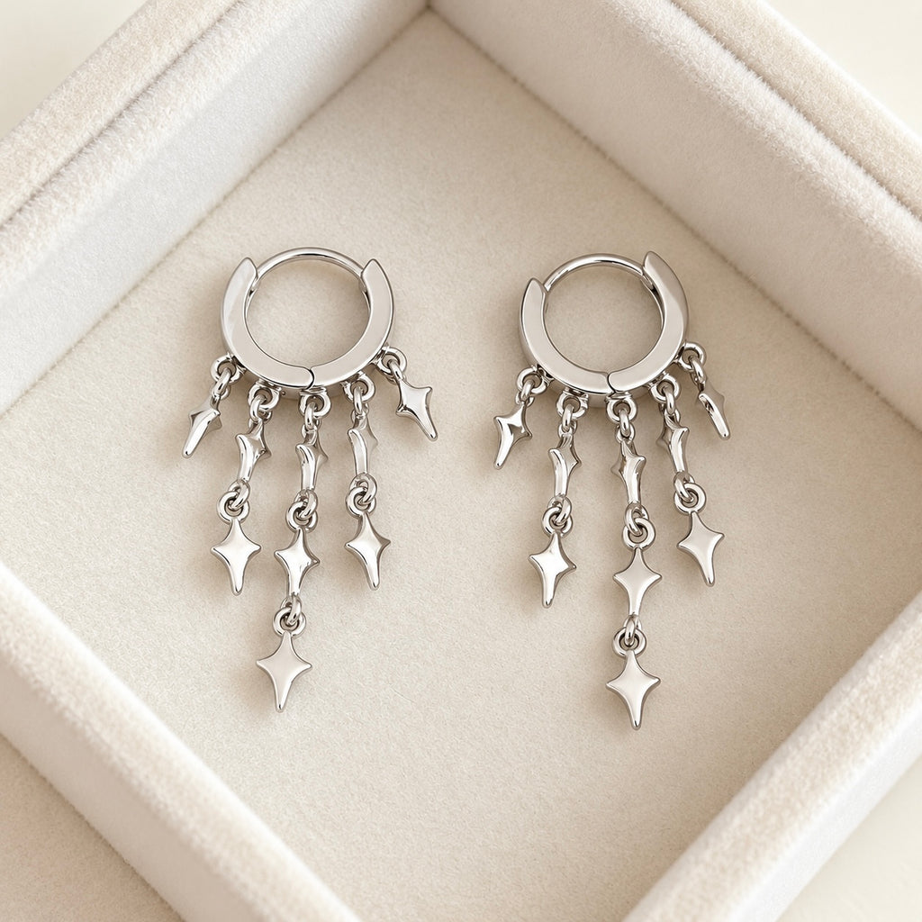 Front view of two star charm huggie earrings on cream velvet