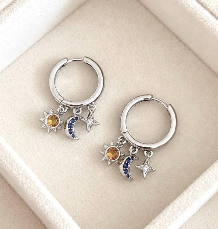 Silver sun moon star charm hoop earrings laid diagonally in a jewellery box