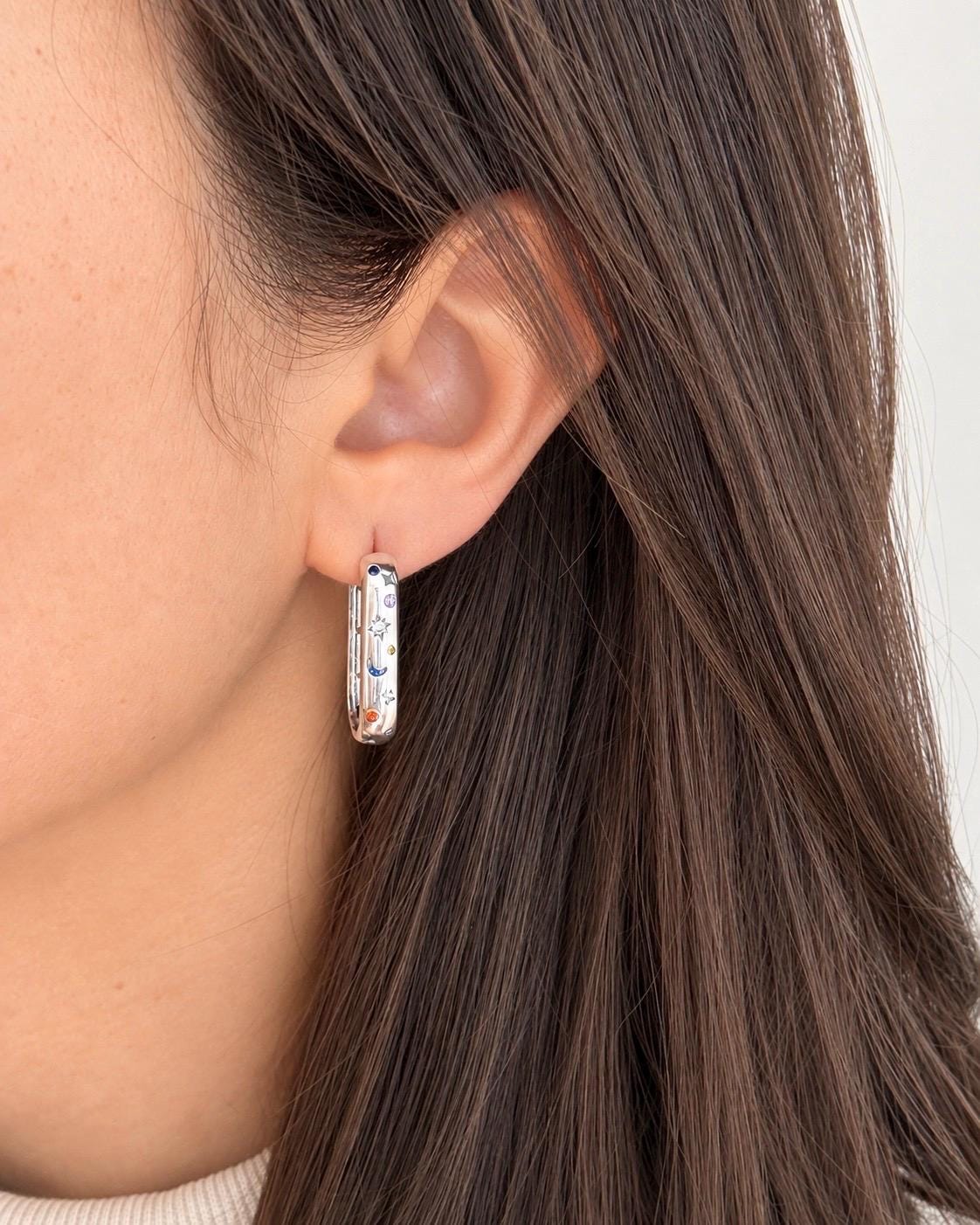 Sterling silver celestial elongated hoop earring worn on ear showing scale and multicoloured sun moon star details