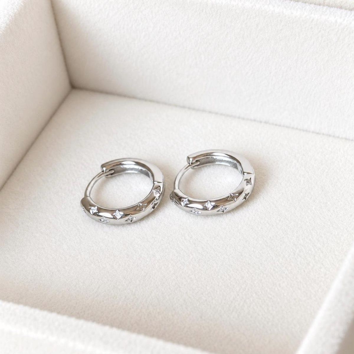Close-up of star engraved CZ hoop earrings on ivory fabric