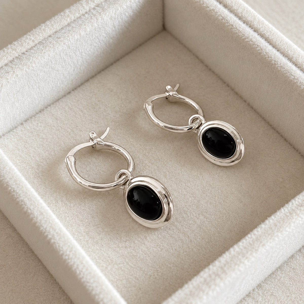 Pair of polished silver black agate oval drop hoop earrings in a cream jewellery box