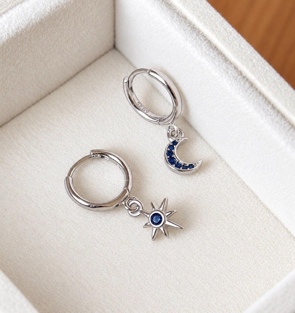 925 sterling silver moon and star mismatched blue cubic zirconia huggie earrings displayed on cream velvet