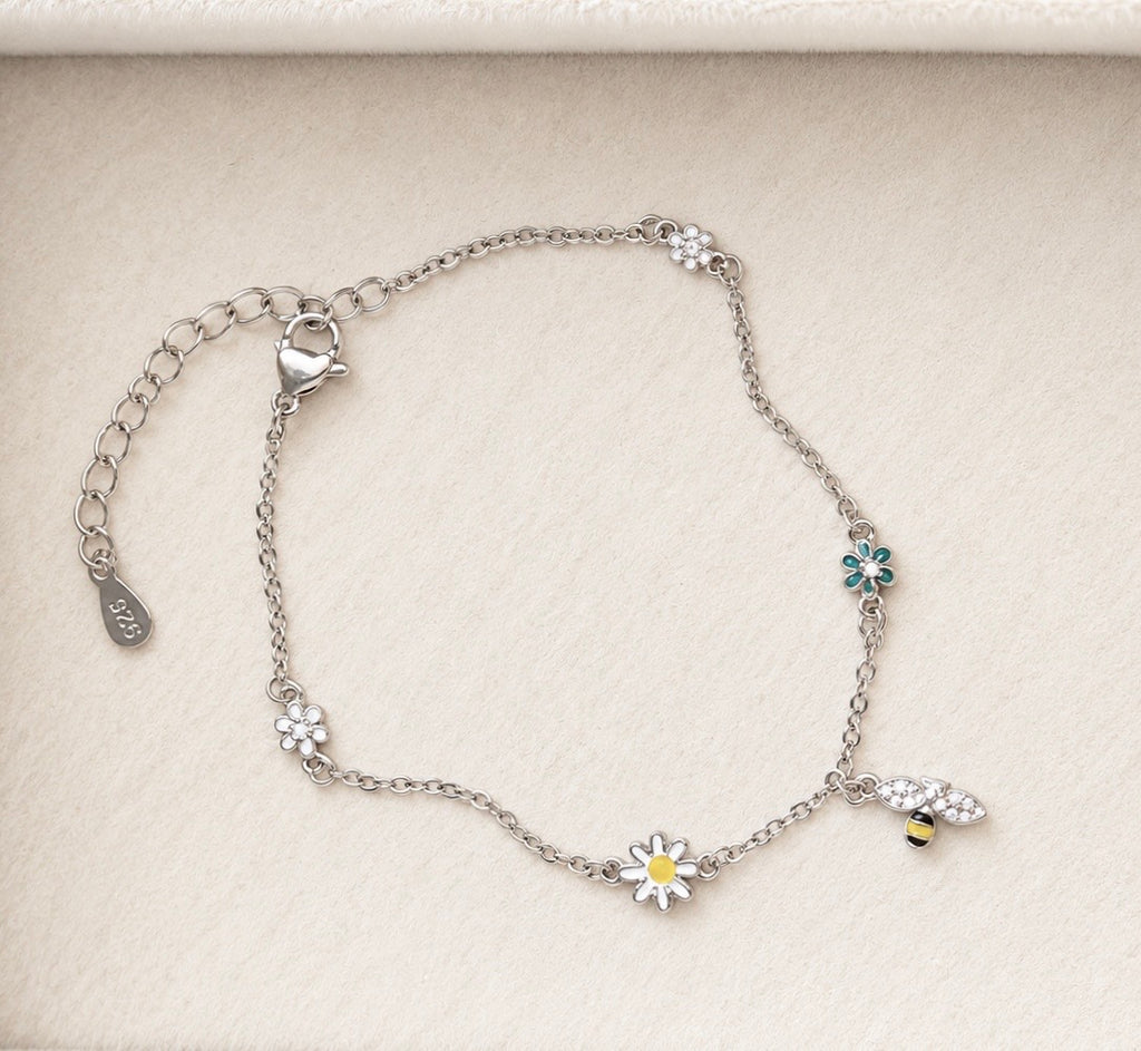 Sterling silver daisy and bee charm bracelet with delicate floral motifs on ivory velvet