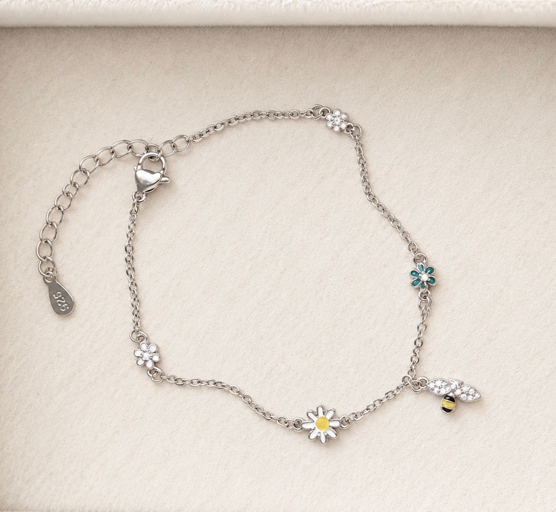 Sterling silver daisy and bee charm bracelet with delicate floral motifs on ivory velvet