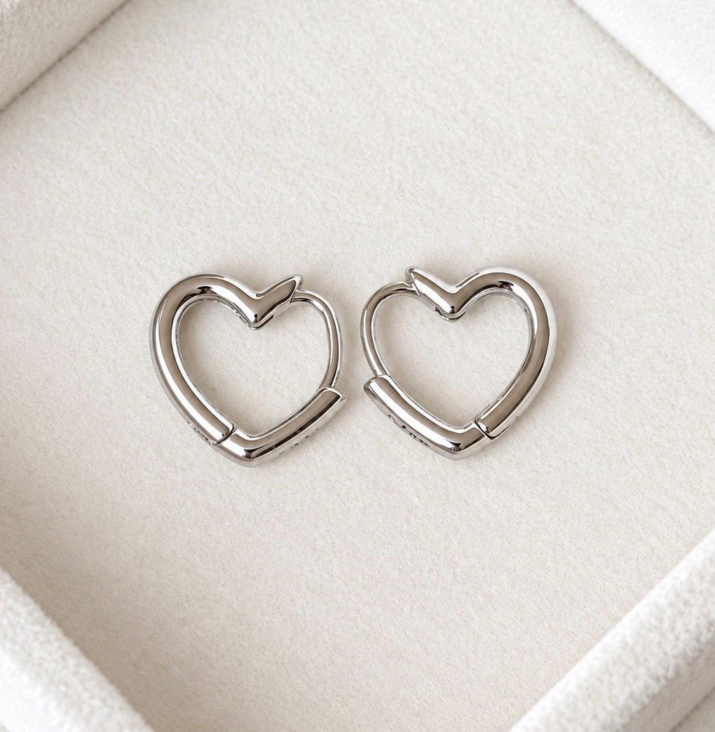 Pair of 925 sterling silver open heart hoop earrings on a cream jewellery display