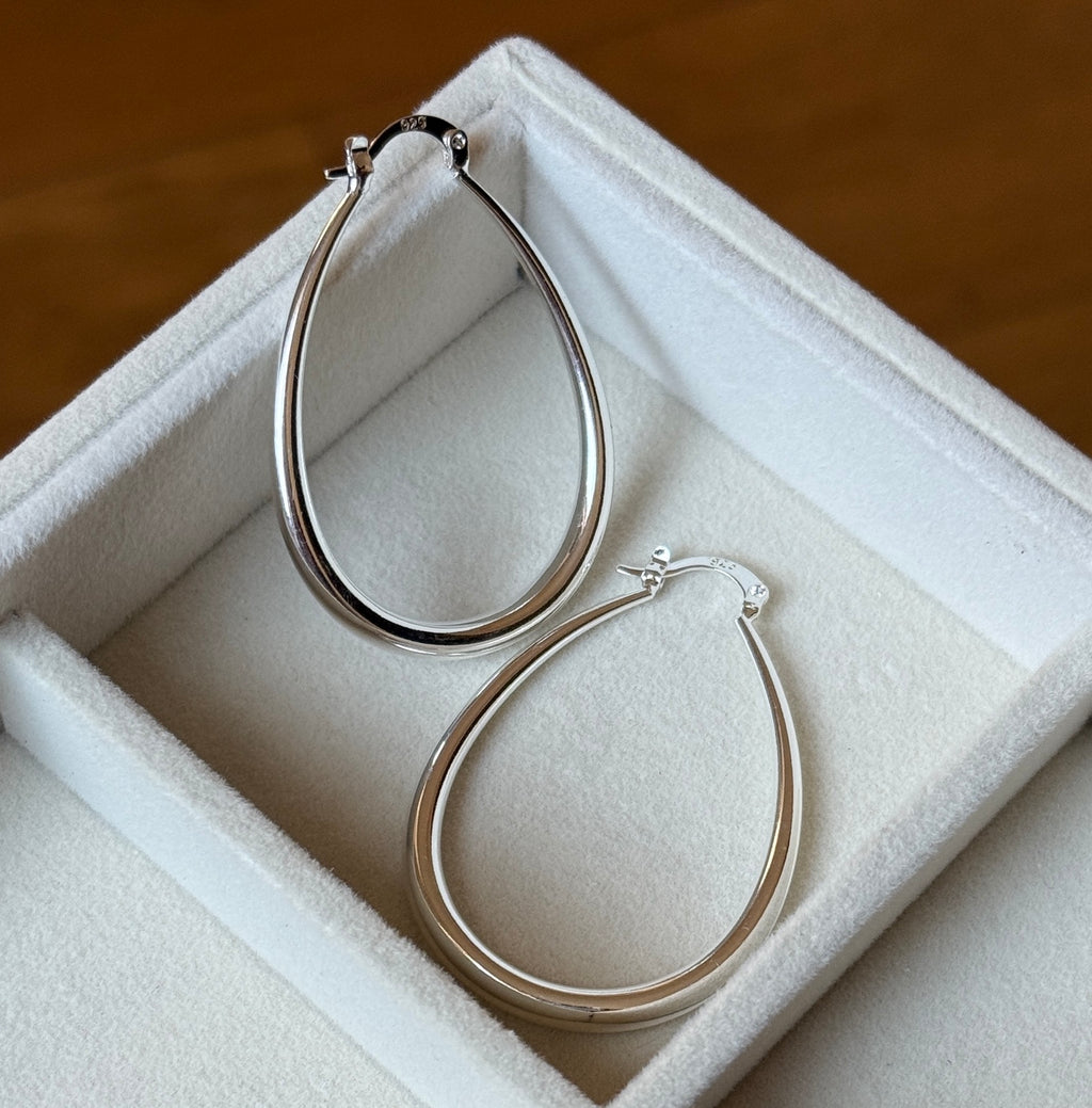 Pear-shaped sterling silver hoop earrings shown at an angle on velvet tray
