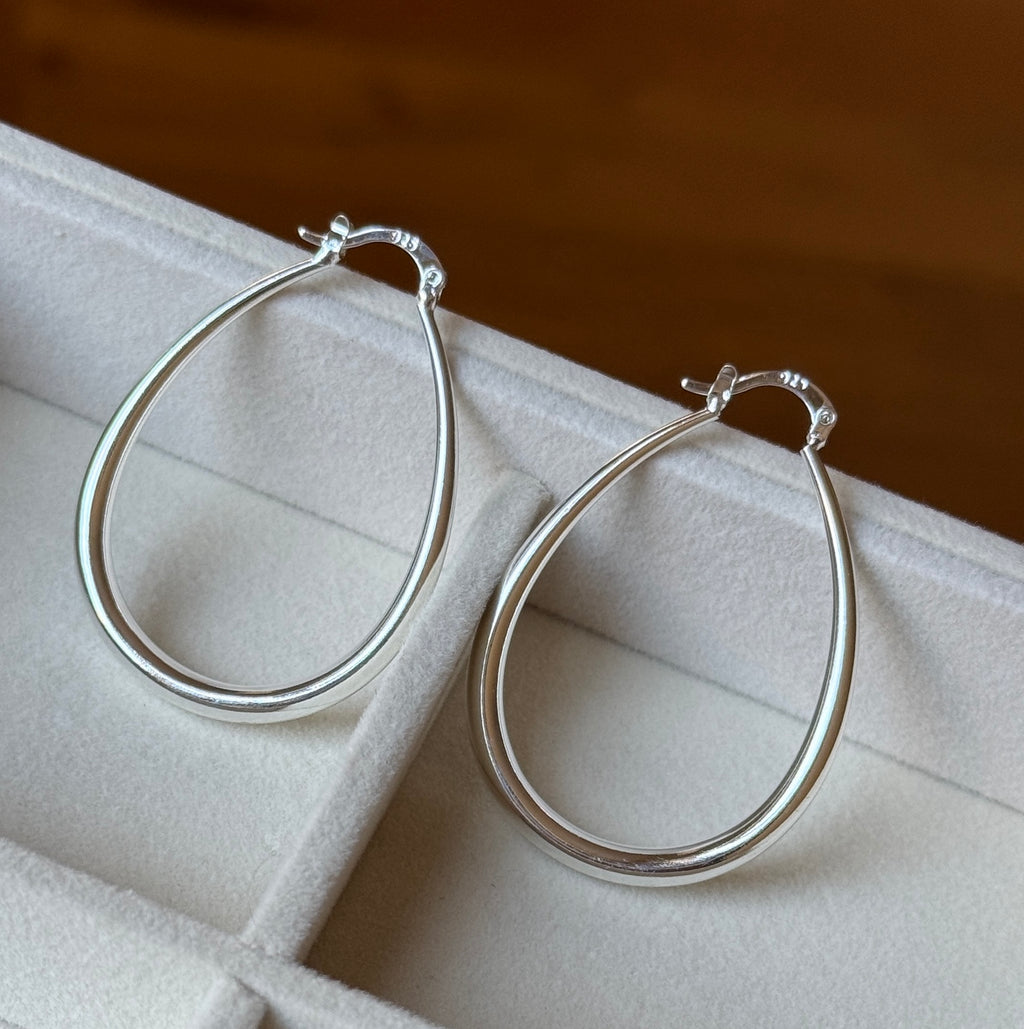 Close-up of two long polished silver teardrop hoop earrings