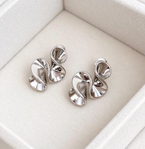 Pair of polished silver-colour abstract sculptural swirl stud earrings on soft cream velvet
