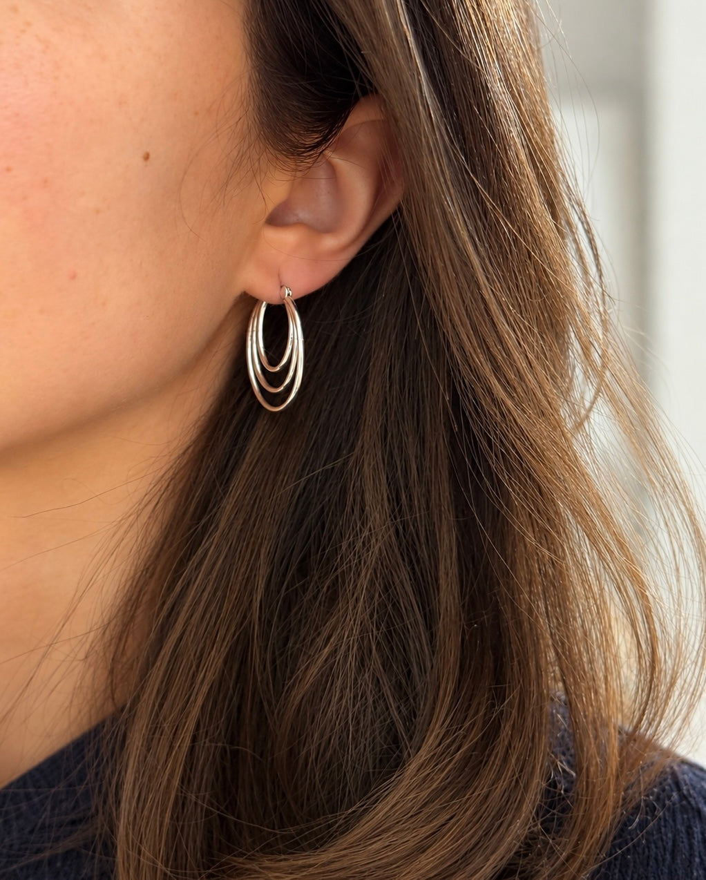 Silver triple-layer oval hoop earring worn on the ear