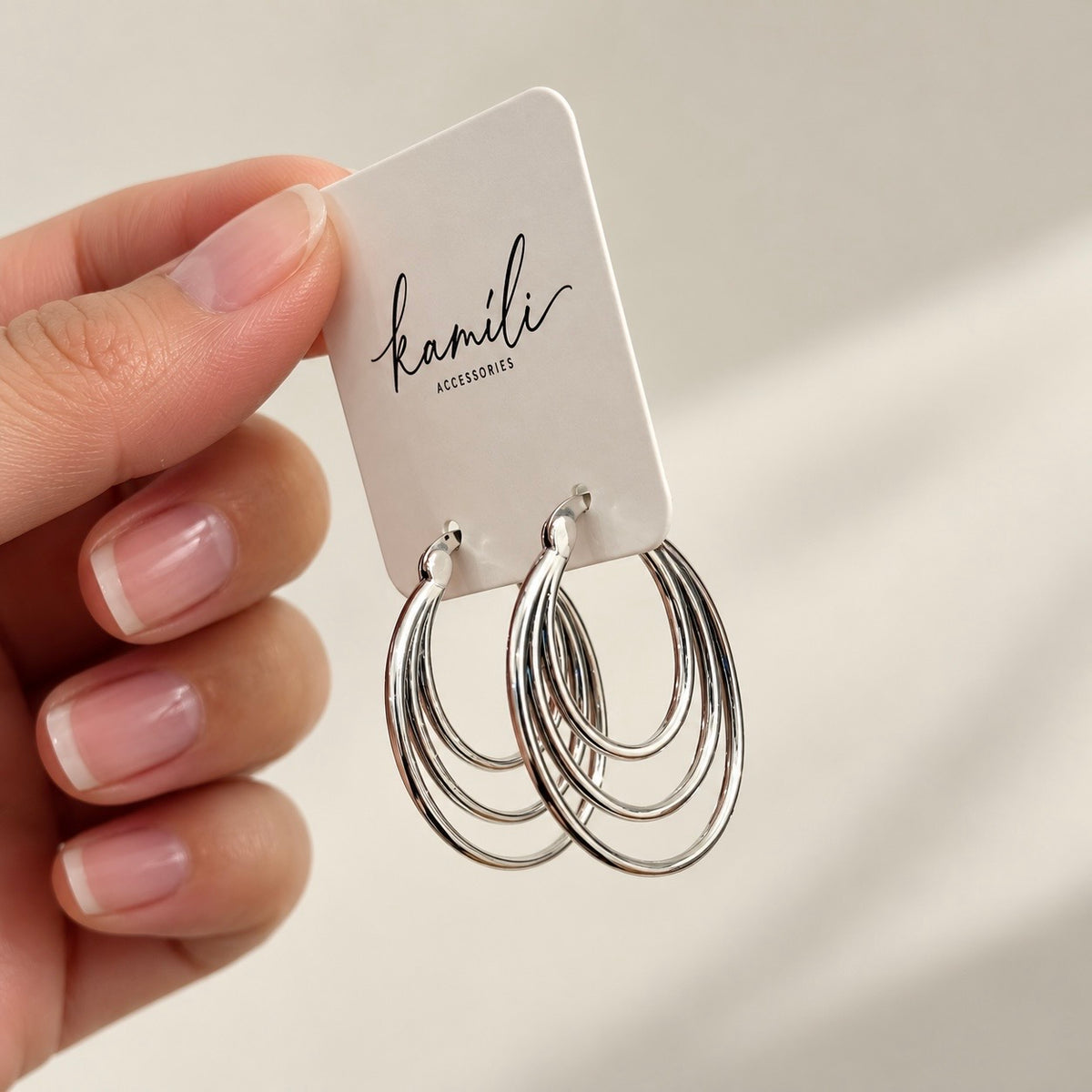 Triple-layer silver oval hoop earrings on a branded card held in hand