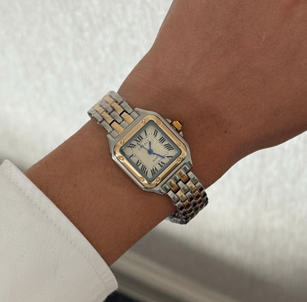 Gold and silver square bracelet watch worn on the wrist against a neutral background